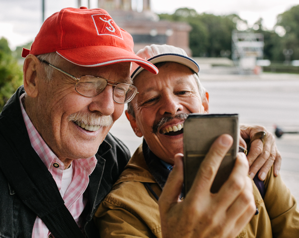 Two elderly men embracing taking selfie with a cell phone.